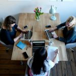 three women sitting around table using laptops