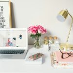 MacBook Air beside gold-colored study lamp and spiral books