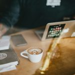 cappuccino art on white ceramic mug beside MacBook Air