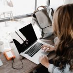 girl wearing grey long-sleeved shirt using MacBook Pro on brown wooden table